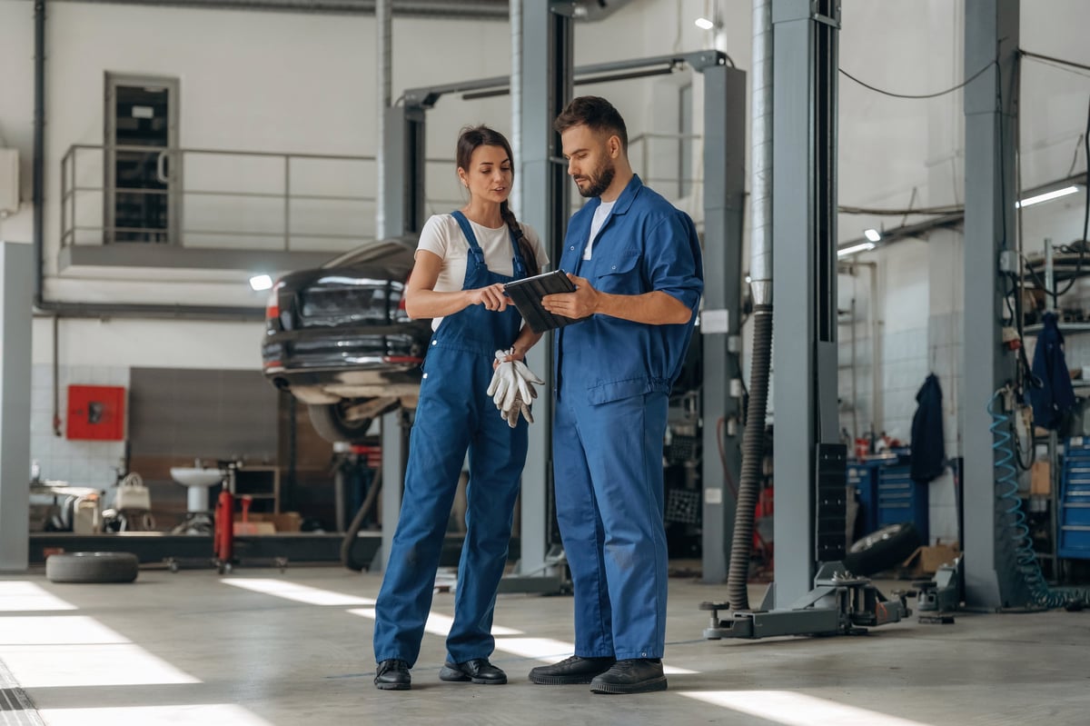 Data is in the digital tablet. Auto repair shop employees are working together. Man and woman.