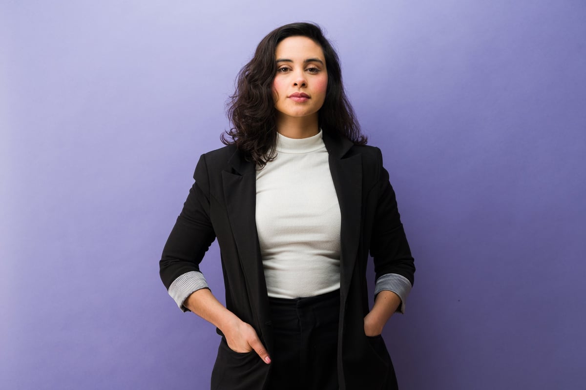 Professional young businesswoman standing in a studio, wearing a black blazer and white top, portraying confidence and professionalism