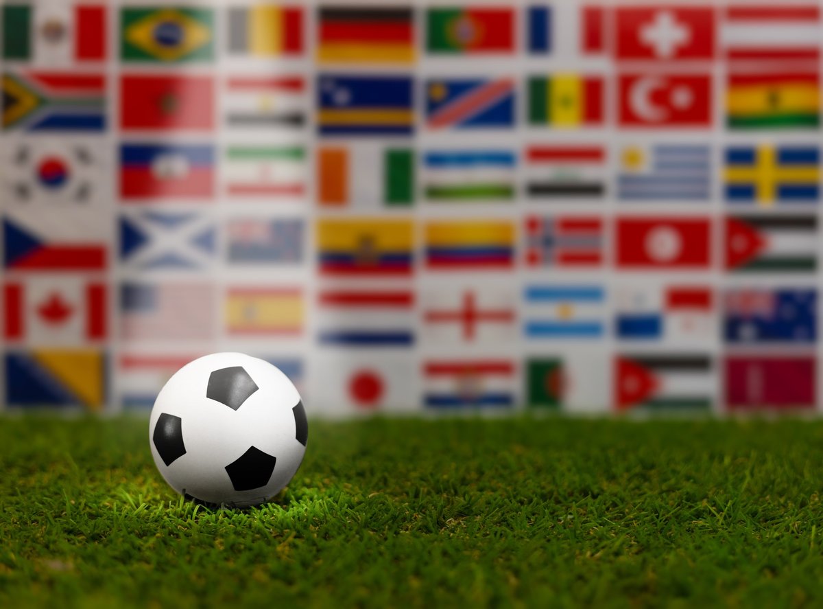 Soccer ball surrounded by international flags on green grass
